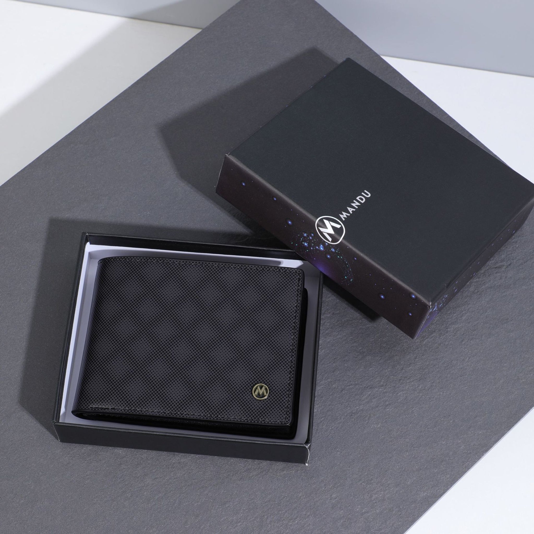 Black wallet with diamond pattern in a box on a gray surface, brand 'Mandu' visible