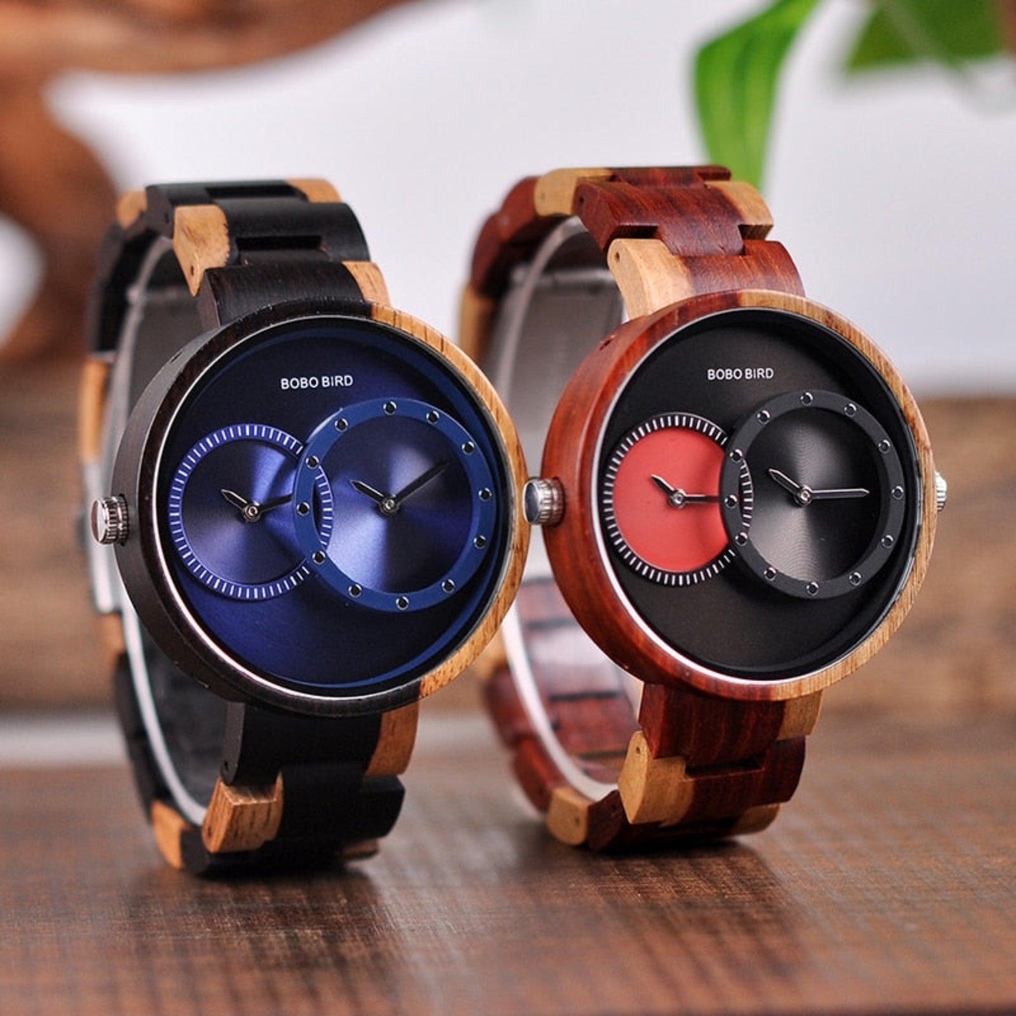 Two wooden watches with blue and red faces on a wooden surface.