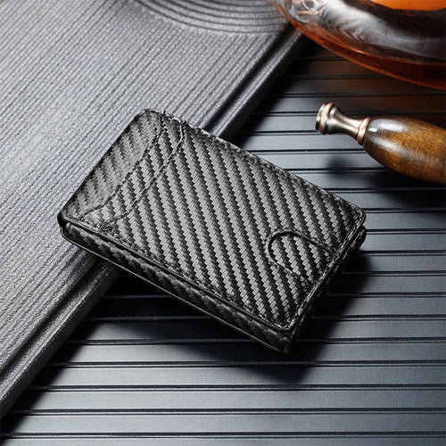 Black carbon fiber wallet on a textured surface with a book and bottle in the background